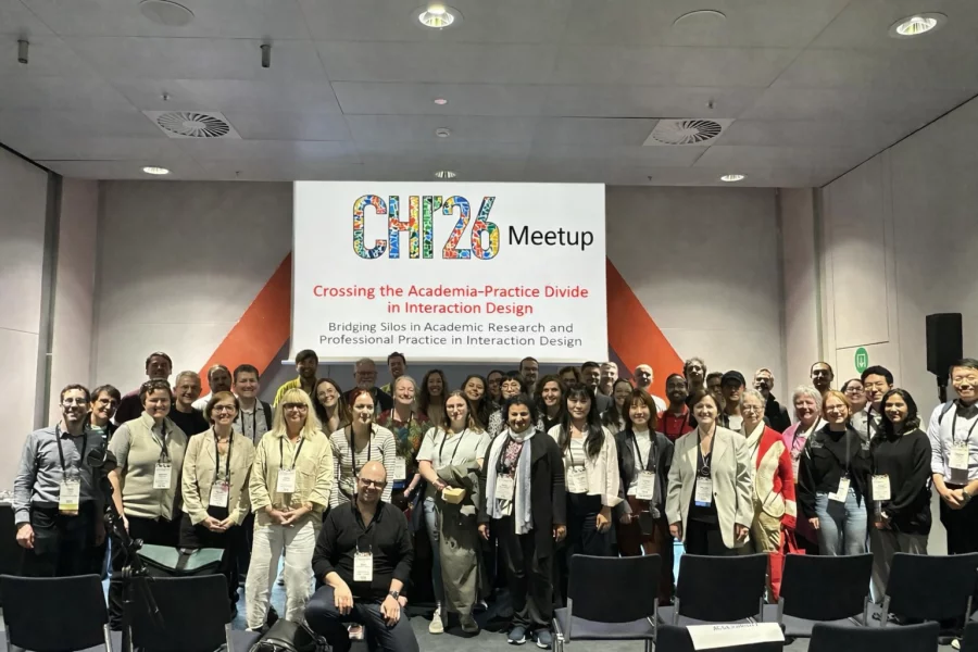 A large group of conference attendees, including Open Home Foundation researchers Annika Schulz and Idil Bostan, pose for a photo in front of a screen displaying "CHI '26 Meetup — Crossing the Academia-Practice Divide in Interaction Design: Bridging Silos in Academic Research and Professional Practice in Interaction Design."